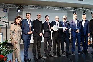 Foto von mehreren Personen, die auf einer Bühne stehen und einen Schlüssel halten. 