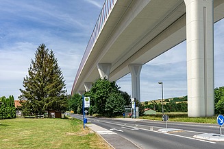 Foto einer neuen Talbrücke von unten gesehen, daneben verläuft eine Landstraße