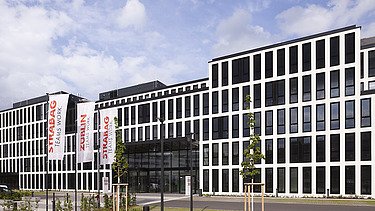 Das Foto zeigt das neue Konzernhaus in Köln, ein modernes Gebäude, fünstöckig mit vielen Feinstern, davor eine Grünfläche