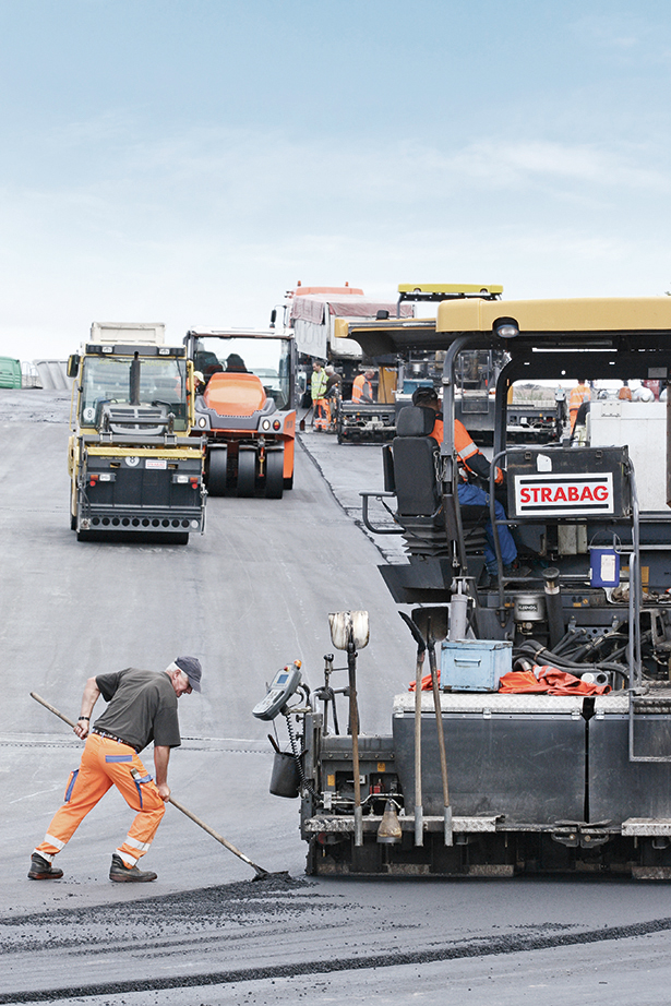 Foto von mehreren Straßenbaumaschinen und einem Arbeiter mit einer Schaufel