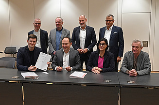 Foto von mehreren freundlich schauenden Personen die an einem Tisch sitzen. 