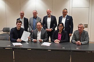 Foto von mehreren freundlich schauenden Personen die an einem Tisch sitzen. 