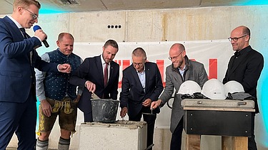 Foto von mehreren Männern im Anzug, die Beton in einen Stein verstreichen. 