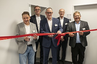 Foto von mehreren Personen die ein Einweihungsband durchschneiden.  