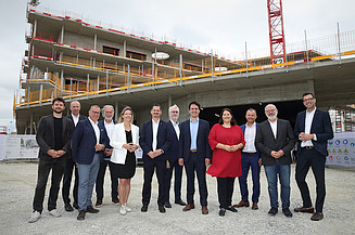Foto von einer Gleichenfeier, mehrere Personen stehen vor einem Rohbau