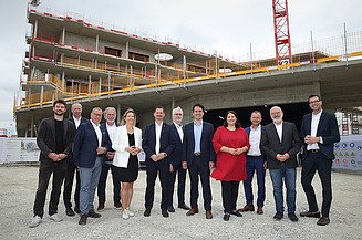 Foto von einer Gleichenfeier, mehrere Personen stehen vor einem Rohbau