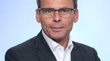Portrait von einem Mann im Anzug mit Brille. 