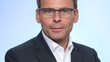 Portrait von einem Mann im Anzug mit Brille. 