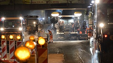 Foto von Straßenbaumaschinen im Einsatz auf einer Fahrbahn bei Nacht