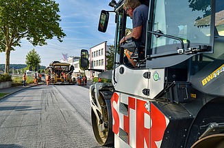 Foto einer Straßenbauschine von der Seite, im Hintergrund eine weitere Maschine