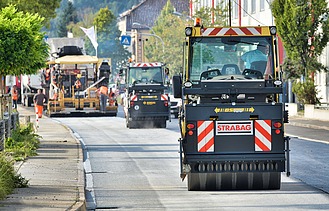 Das Bild zeigt eine gerade Straße auf der mehrere Straßenbaumaschinen hintereinander fahren