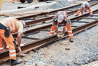 Foto von drei Schienenbauarbeitern beim Schienenverlegen