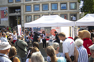 Foto von einem ZÜBLIN-Stand, wo eine Reportage von einem Roboter gedreht wird. Drumherum sind viele Personen versammelt    