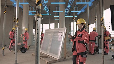 Foto von einer Baustelle in einem Gebäude. Es sind mehrere Personen mit Schutzausrüstung zusehen. Die Decke wird von Stangen getragen.   