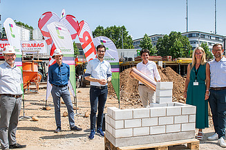 Foto von mehren Personen, die eine symbolische Grundsteinlegung durchführen. 