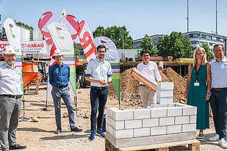 Foto von mehren Personen, die eine symbolische Grundsteinlegung durchführen. 