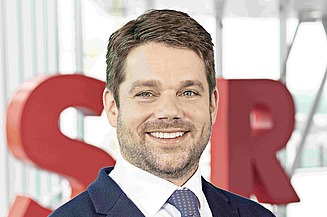 Photo of Klemens Haselsteiner standing in front of the red letters STRABAG