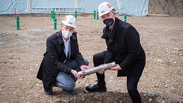 Foto von zwei Männern die eine Zeitkapsel vergraben.  