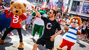 Foto von tanzenden Maskottchen und einem Animator. Drumherum sind viele Menschen.  