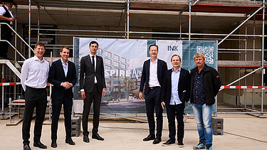 Foto von mehreren schick gekleideten Personen auf einer Baustelle.