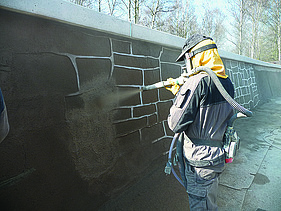  Foto von einer Person, die eine Wand mit brauner Farbe besprüht.