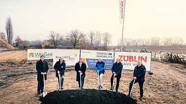 Foto von mehreren Männern, die einem Sparten in die Erde stecken. Sie schauen glücklich. 