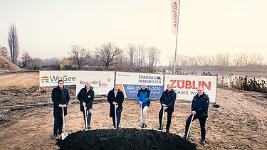 Foto von mehreren Männern, die einem Sparten in die Erde stecken. Sie schauen glücklich. 