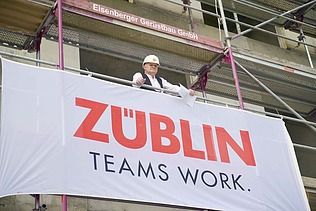 Mann steht auf einem Gerüst einer Baustelle. Vor ihm ist das ZÜBLIN Banner. 
