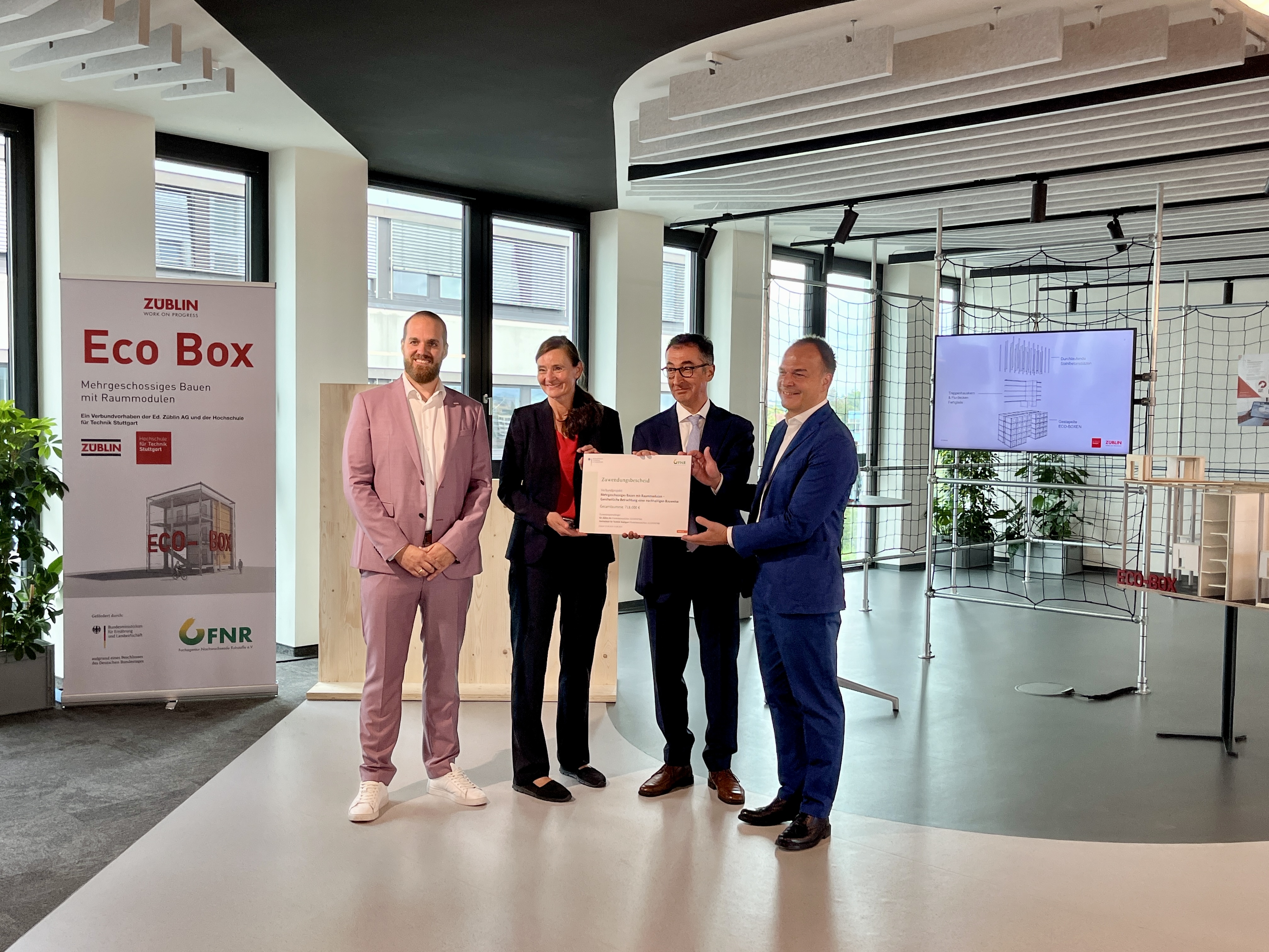 Foto von vier Personen die schick gekleidet sind. Sie halten einen Zertifikat. 