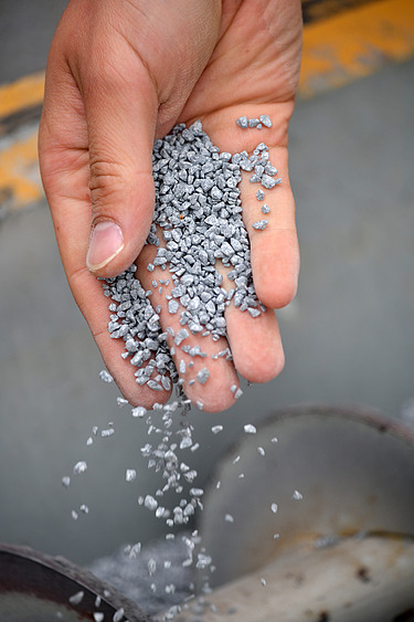 Foto einer Hand, die graue Kügelchen runter rieseln lässt