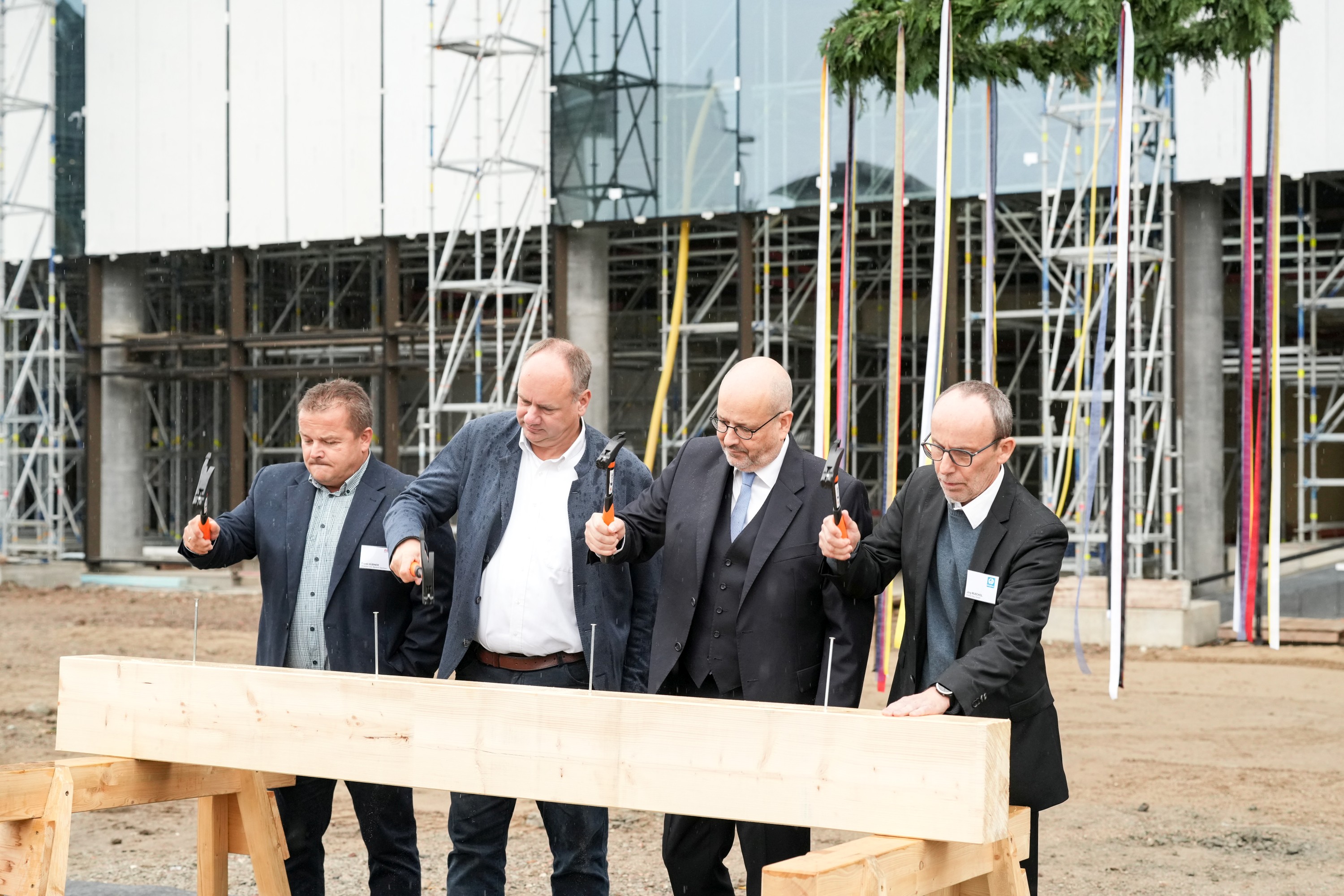 Foto von vier Männern die einen Nagel in ein Holzbrett hauen.  