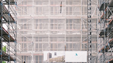 Foto von mehren Personen auf einer Baustelle. Auf einem Gerüst wird der Richtspruch verkündet. 
