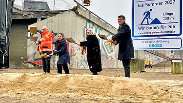 vier Personen schaufeln Sand