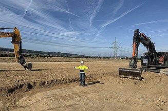 Foto von zwei Bauarbeitern mit einer Maschine bei Tiefbauarbeiten in einem Graben