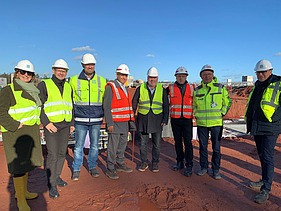 Foto von mehreren Personen die in Warnwesten auf einer Baustelle stehen.  