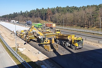 Das Bild zeigt eine nähere Ansicht von mehreren Straßenbaumaschinen beim Einbau einer Betondecke