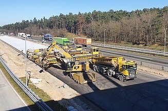 Das Bild zeigt eine nähere Ansicht von mehreren Straßenbaumaschinen beim Einbau einer Betondecke