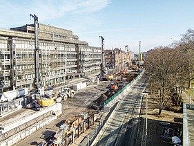Foto von einer aufgerissenen Straße. Es sind mehrere Kräne und andere Baugeräte zusehen.