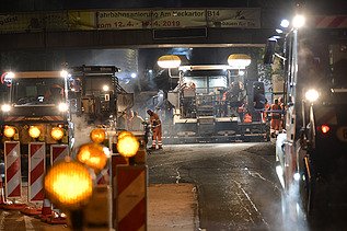 Foto von Straßenbaumaschinen im Einsatz auf einer Fahrbahn bei Nacht