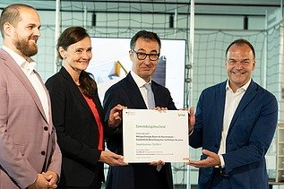 Nahaufnahme von vier Personen die schick gekleidet sind. Sie halten ein Zertifikat. 