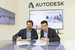 Foto von zwei Personen bei einer Vertragsunterzeichung, dahinter ein Bildschirm, darüber die Aufschrift Autodesk