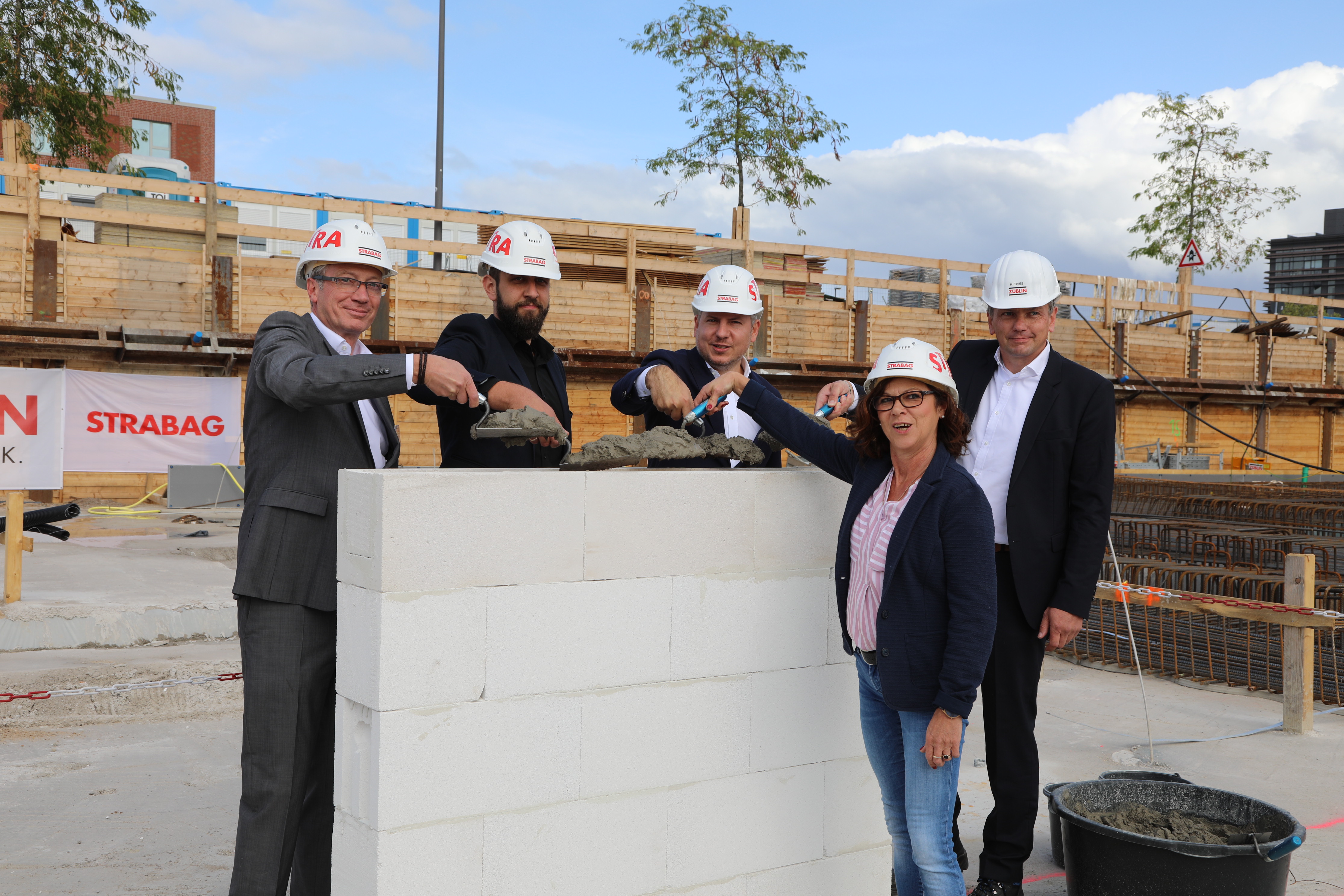 Foto von vier Personen in Anzug, die auf einer kleinen Mauer Beton verteilen. 