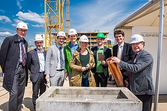 Foto von einer Frau und mehreren Männern auf einer Baustelle, bei symbolischer Grundsein für das JobRad-Firmenzentrale. Ein Mann hält eine Röhre. 