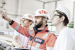 The picture shows three people wearing white construction helmets with the inscription STRABAG