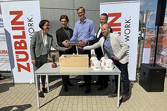 Foto von mehreren Personen, die eine Röhre halten bei der Grundsteinlegung.  