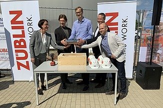 Foto von mehreren Personen, die eine Röhre halten bei der Grundsteinlegung.  