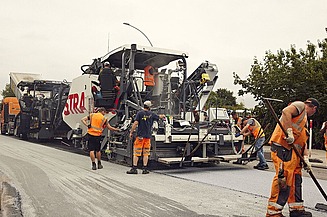 Foto von mehreren Straßenbauarbeitern rund um eine große Asphaltbaumaschine