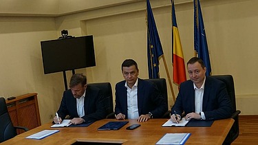 Foto einer Vertragsunterzeichnung mit drei Personen, die an einem Tisch sitzen