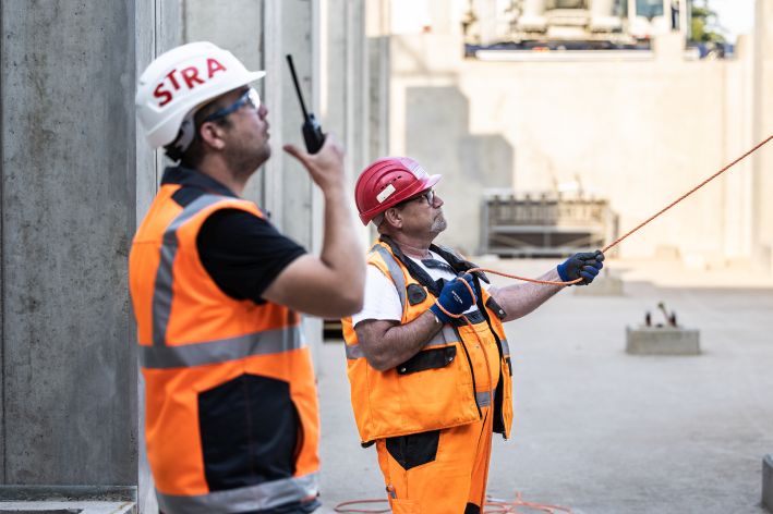 Foto von zwei Arbeitern, der vordere hält ein Walkie-Talkie, der hintere ein Kabel in der Hand