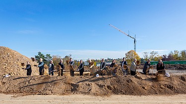 Foto von mehreren Männern auf einer Baustelle die mit einen Sparten Erde in die Luft werfen. 